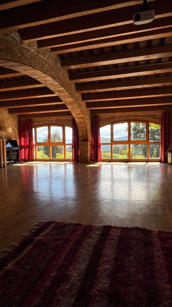 Sala de prácticas de la masía — vigas de madera, ventanales y vistas a la montaña